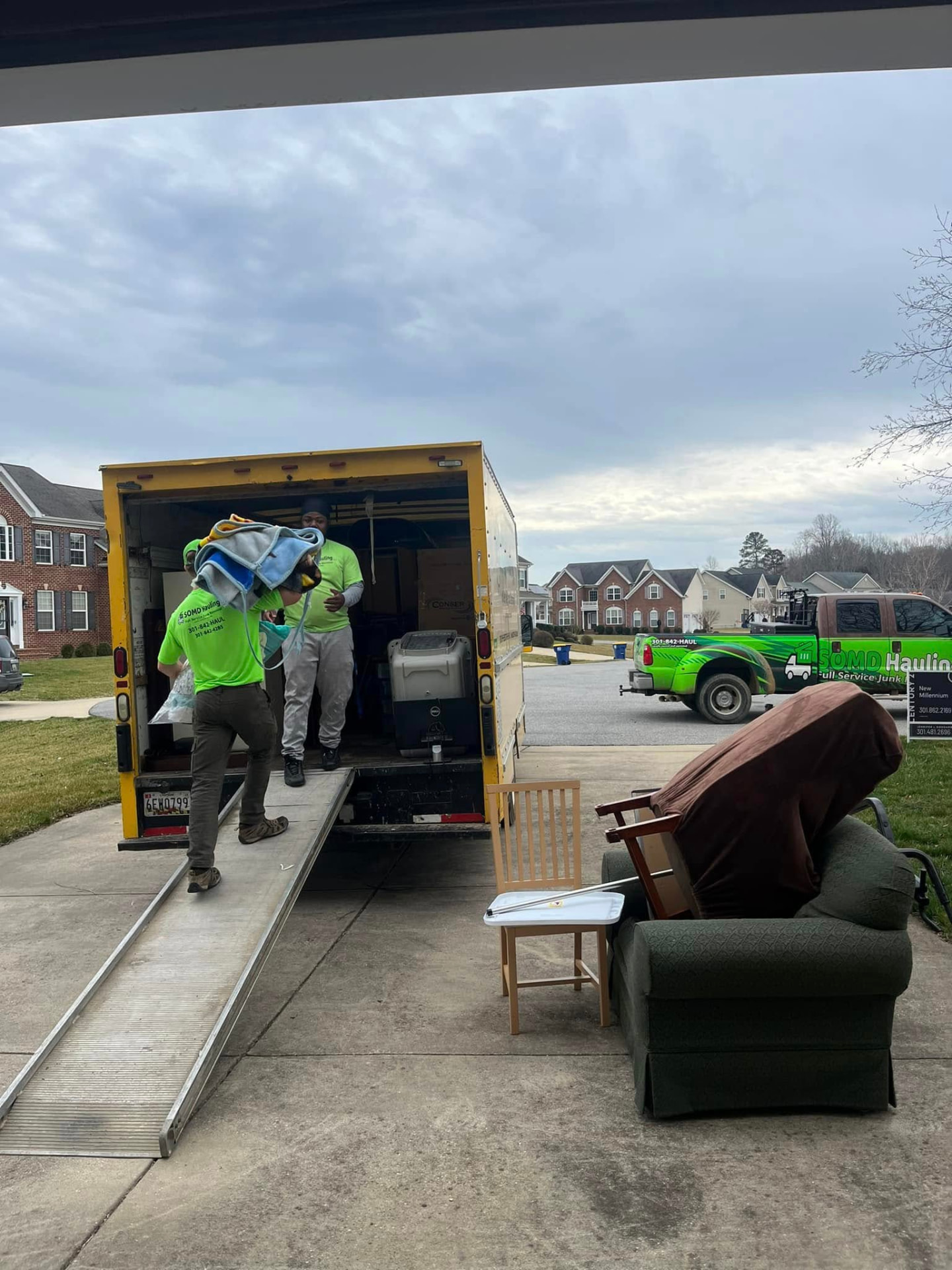 Two workers carrying a heavy item up a truck ramp